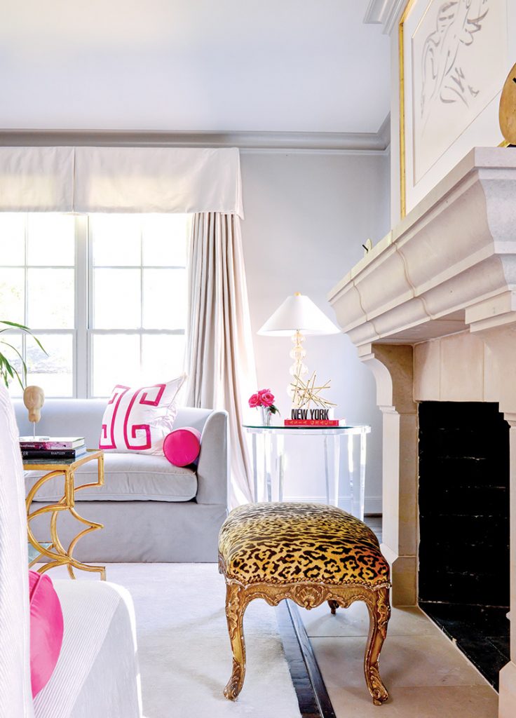 Pink and white sitting room with a limestone mantel and a leopard-topped gilt stool