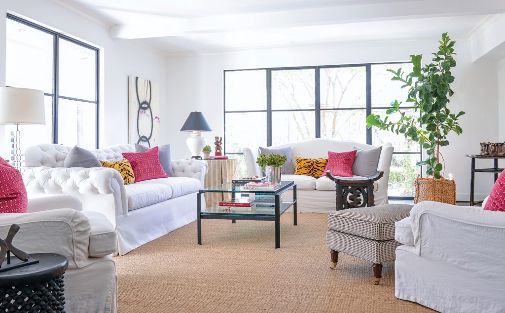 White slipcovered sofas with raspberry pillows before a wall of windows