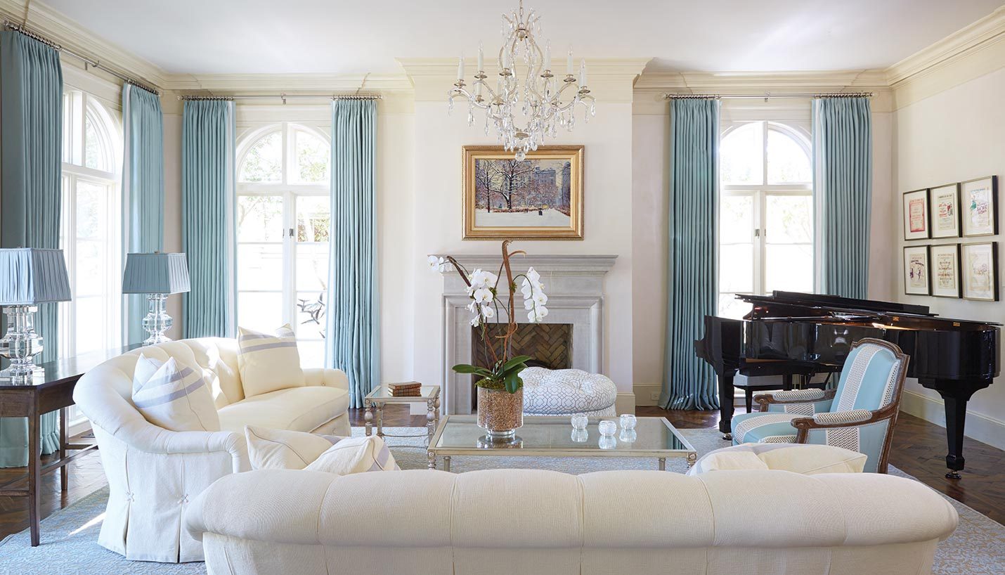 Blue and cream living room with a chandelier, arched windows and a grand piano