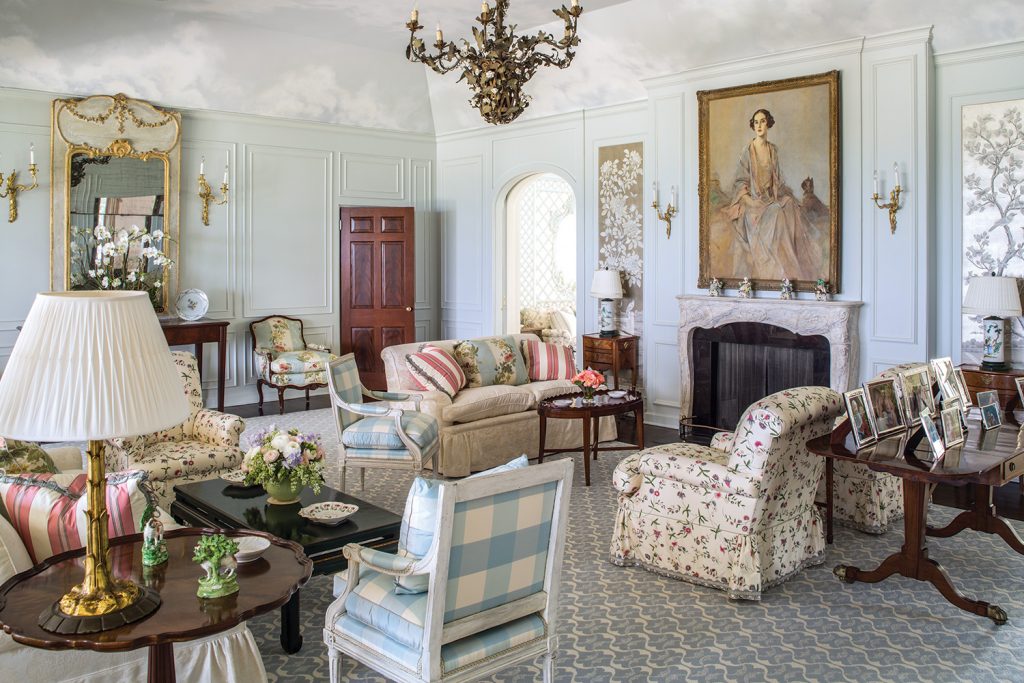 Traditional living room with skirted lamps, a portrait over the mantel and a check armchair