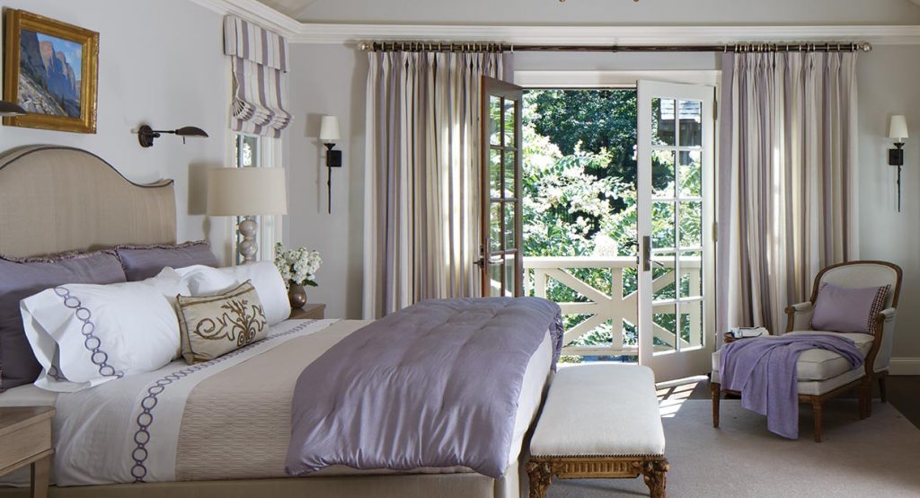 Bedroom with a carved headboard, white linens and a bench at the foot of the bed
