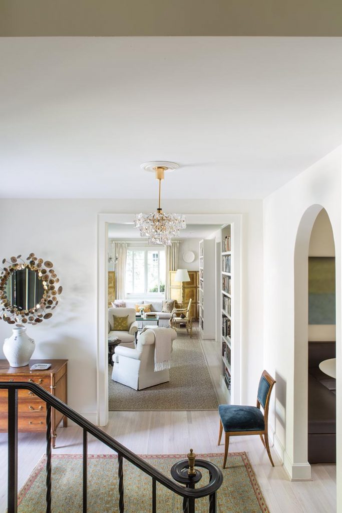 The view from the staircase draws the eye through the entry hall to the living room. The mirror above the entry hall chest is by C. Jere.