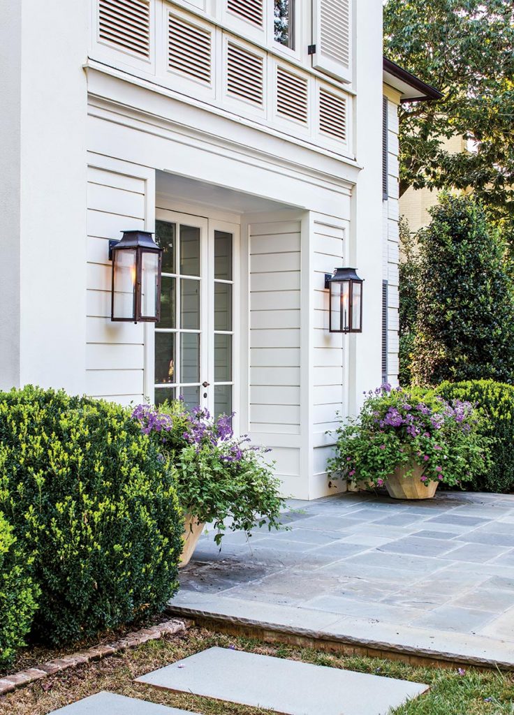 White house entry with lanterns, a lattice panel and boxwoods along a stone walk