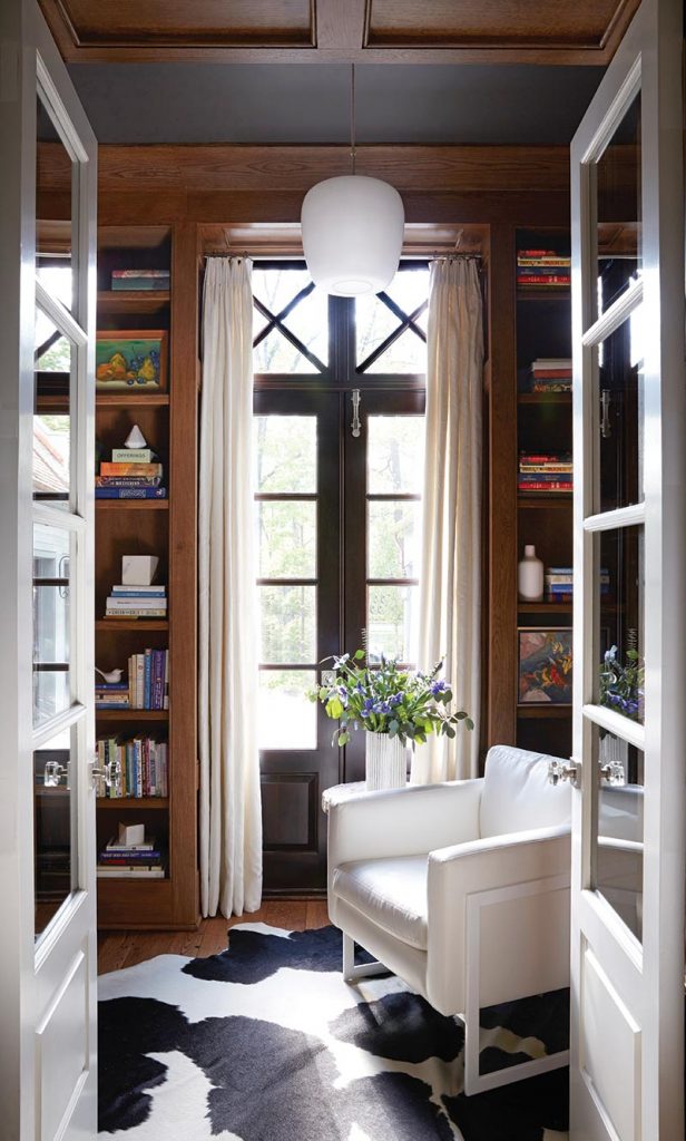 Floor-to-ceiling bookcases combine with a pair of tall French doors to instill a relatively small library with an added sense of importance. Contemporary white furnishings and a cowhide rug counter the room’s natural-wood finishes.