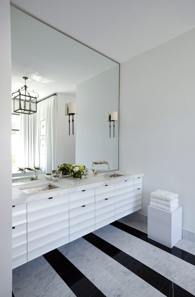 White bath with an oversized mirror, long vanity and a black-and-white striped rug