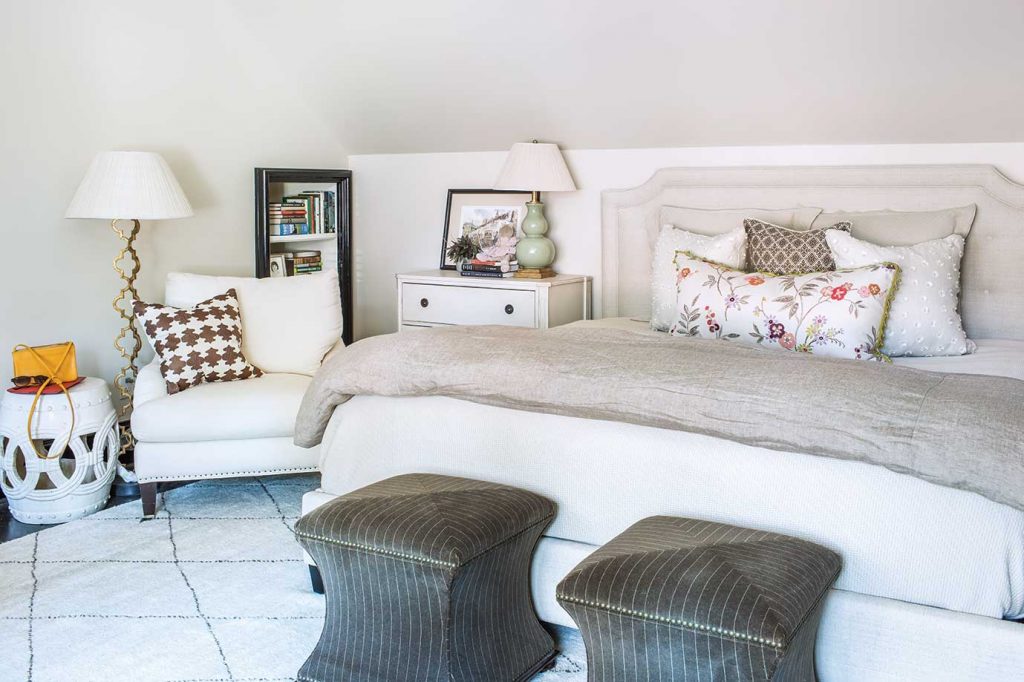 This bedroom speaks to comfort and the power of an overall neutral palette enhanced by patterned pillows, menswear pinstriped ottomans, and a Moroccan rug.