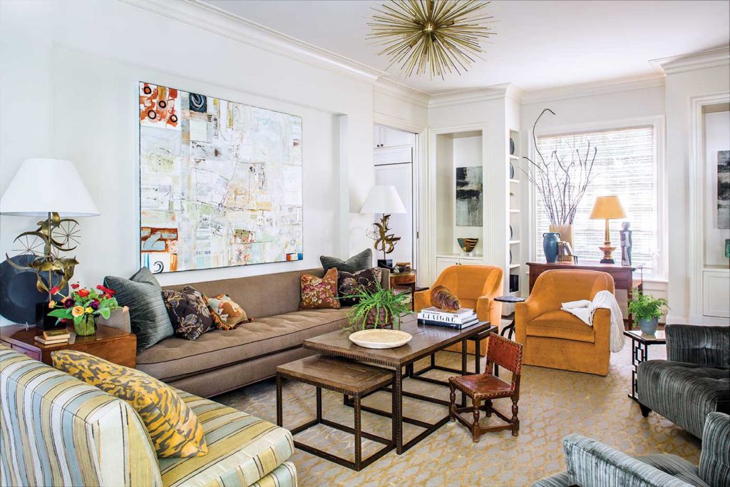 The living room presents an engaging tableau filled with mid-century-inspired pieces and antique accents punctuated by a large contemporary painting, lamps with a bit of whimsy, and textured pillows.