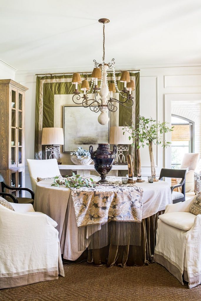Fabrics define the intimate dining room with slipcovered chairs and a layered skirted table. A  19th-century French samovar punctuates the table’s center.