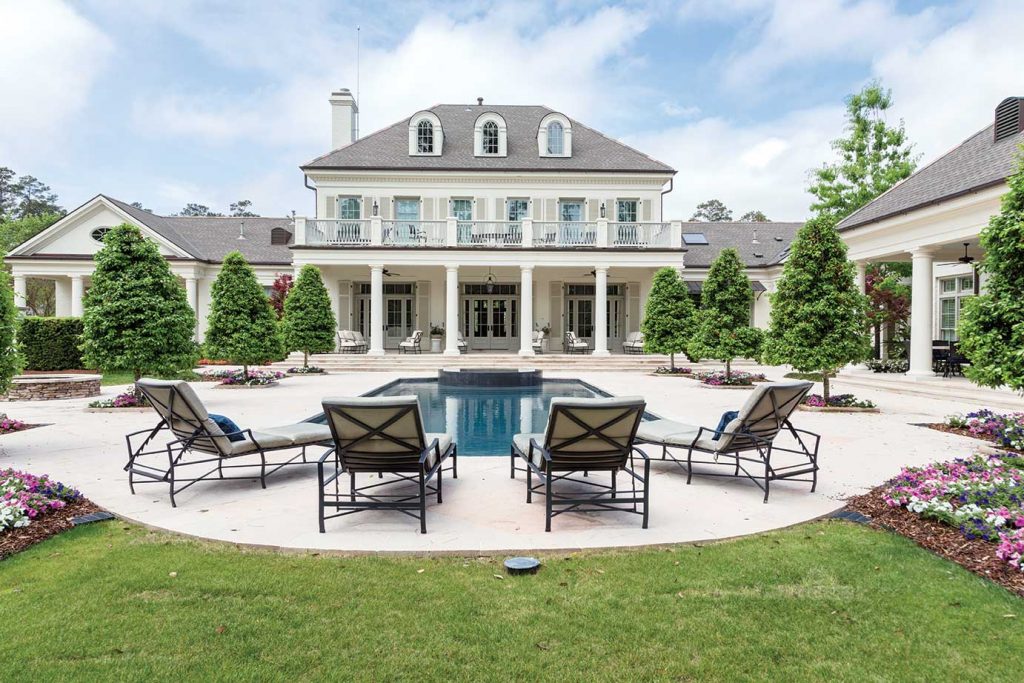 Stone house with a pool terrace, chaises and clipped hedges under a blue sky