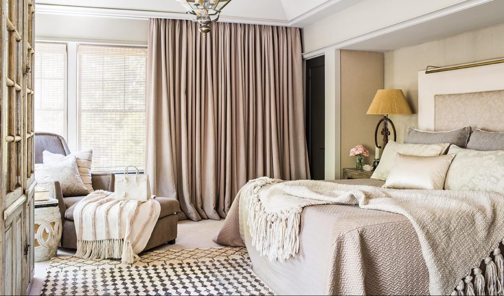 Bedroom in cream and taupe with pinch-pleat curtains and layered throws