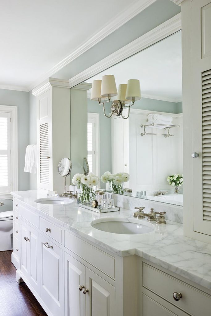 Custom wood paneling and white marble counters create a pristine master bathroom.