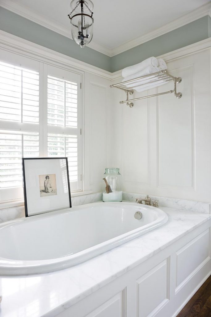 Custom wood paneling and white marble counters create a pristine master bathroom.