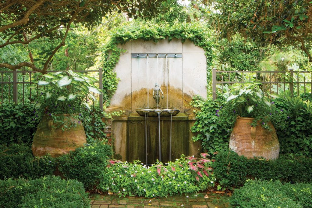 Wall fountain set into a vine-covered garden niche flanked by urns