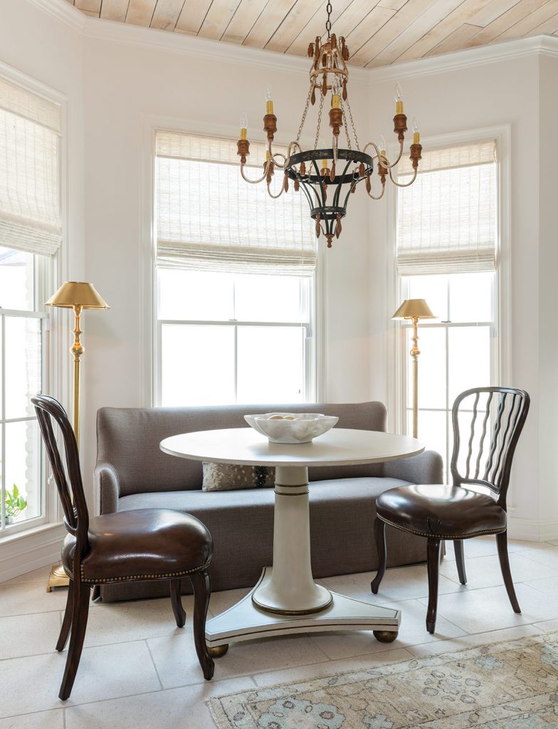 Curved banquette and slipper chairs around a pedestal table in a bay window