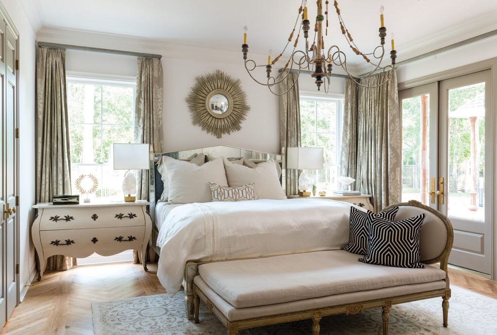 A sophisticated chevron pattern, installed by a local artist, graces the floors of the master bedroom and bath. Antiques and technology live side by side in the form of a French daybed and remote-controlled drapes. An oversized gilded mirror, billowy curtains, and a crystal-laden chandelier add to the romantic appeal of the bathroom.