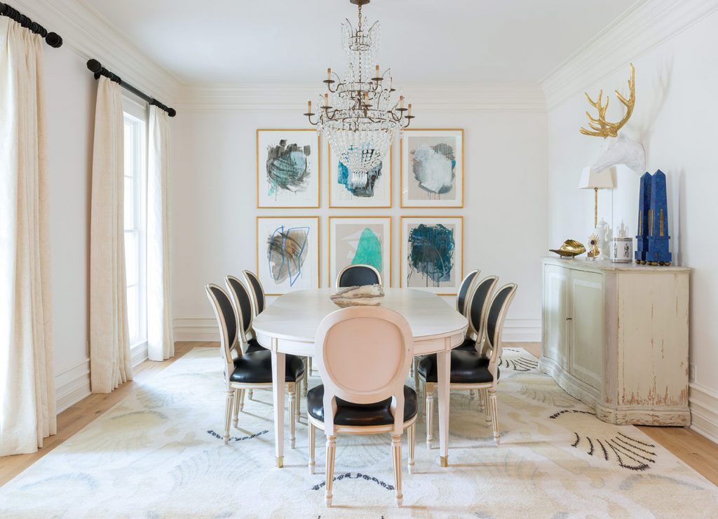 In the dining room, hues both soft and bold combine for a modern spin on art deco décor. The Lillian August dining table sits atop a custom rug by French Accents. Crisp drapery panels are complemented by antique carved ebony-wood finials. A combination of leather and fabric turns classic dining chairs into conversation pieces. The featured artwork is dubbed "Weather Day 2014" and sets the mood for the space and, indeed, the entire home.
