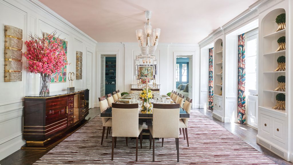 An unexpected shell-pink ceiling casts flattering reflective light from the Murano chandelier in the dining room. Over the sideboard, a painting by Corinne Bizzle brings more color to the space.