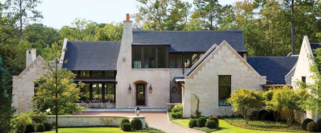 White stone and stucco house with a slate roof set among mature trees