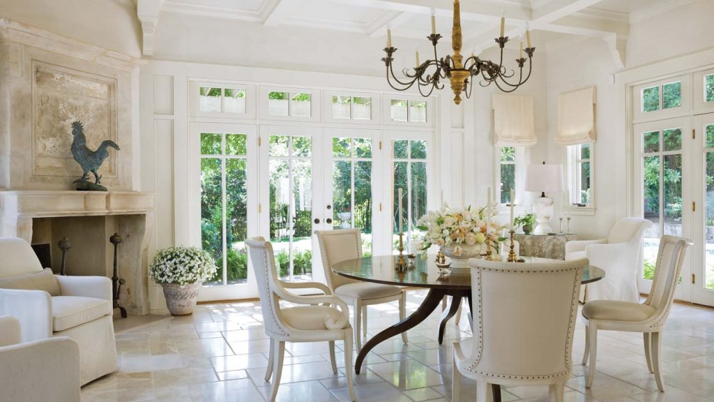 White dining room with French doors, a chandelier and slipcovered chairs