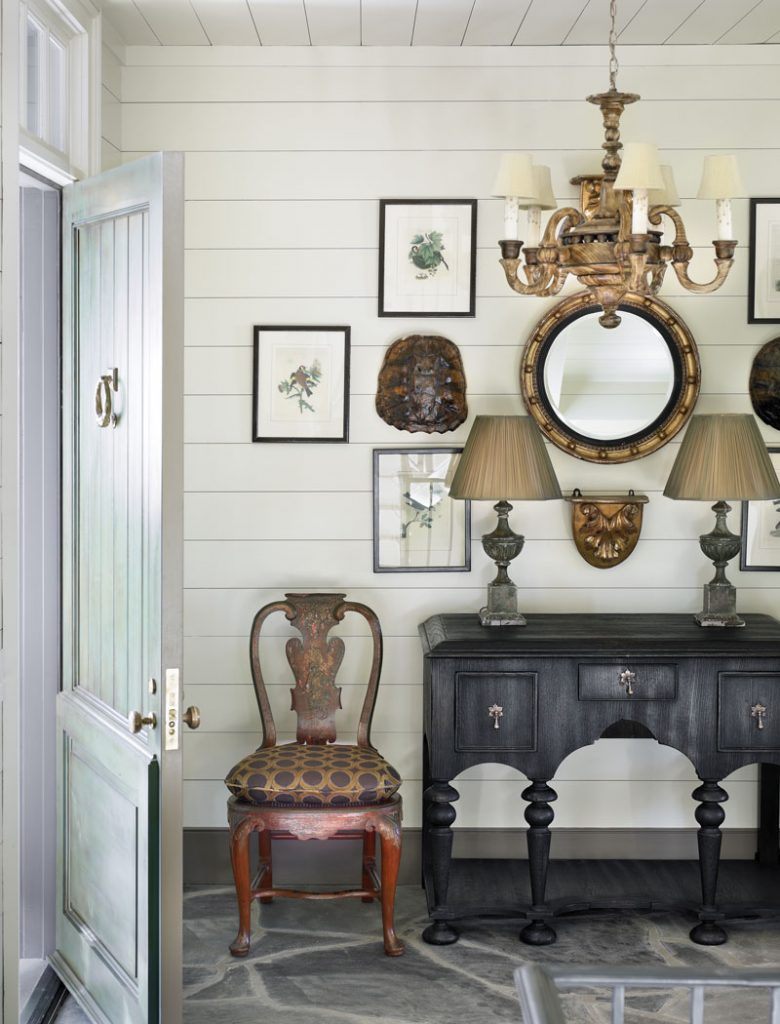 Antique chest below a scalloped mirror on a shiplap wall with framed prints