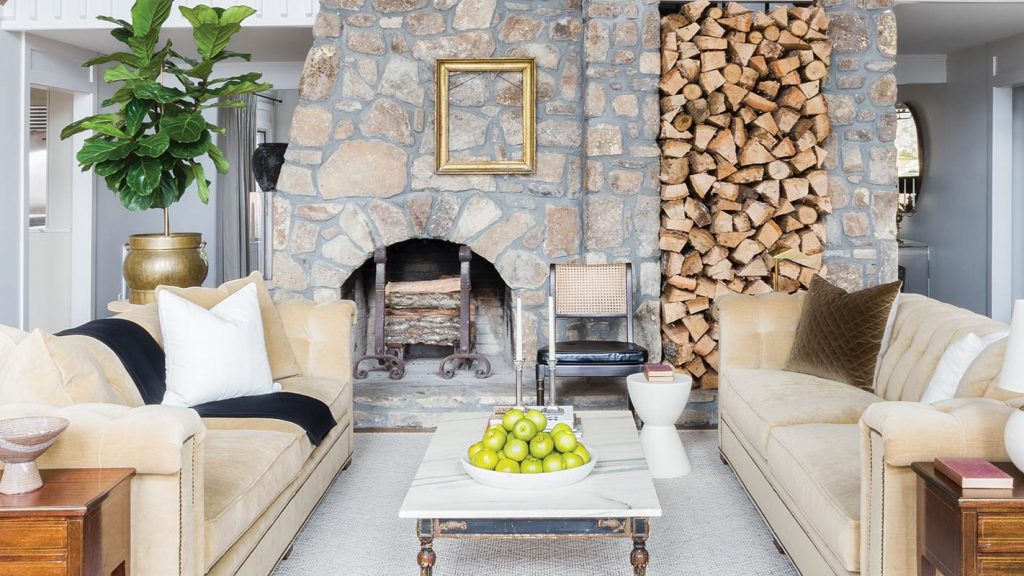 Stone fireplace with stacked firewood between cream sofas and green apples