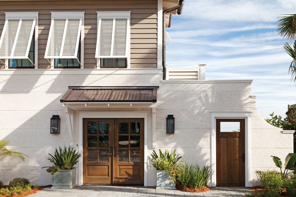 The exterior features a solid masonry facade on the first level that gives way to warm wood siding above. The side gate allows access to outdoor seating and the beach.