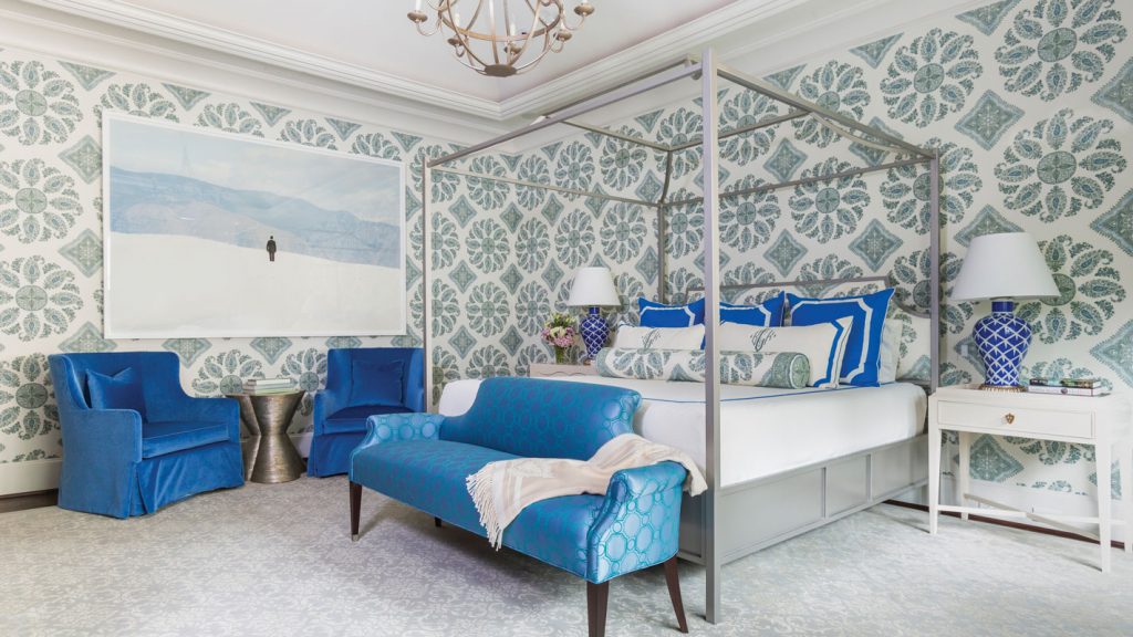 Bedroom with medallion wallpaper, a canopy bed and bright blue chairs