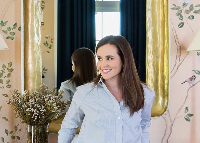 Two women in pale shirts beside a mirror in a hand-painted wallpapered room