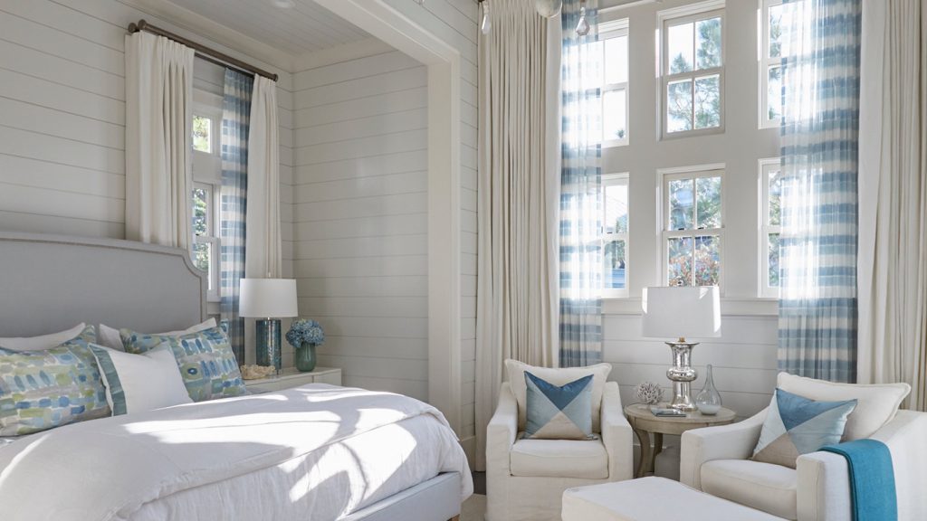 Bedroom with an upholstered headboard, layered blue pillows and paired chairs