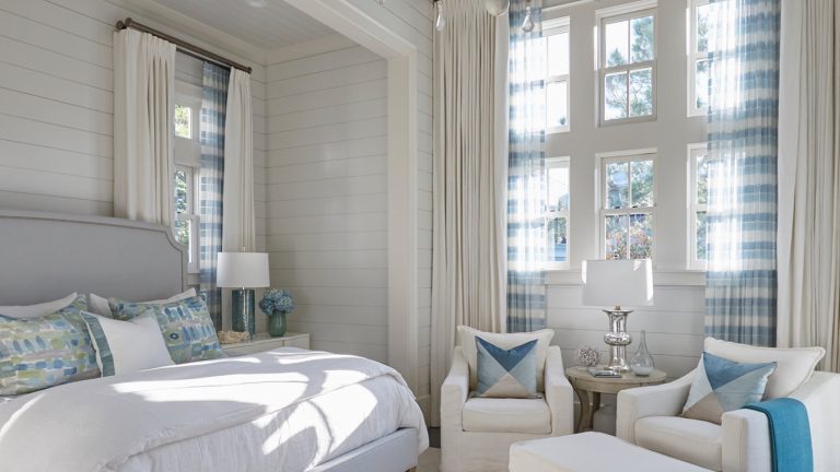 Bedroom with an upholstered headboard, layered blue pillows and paired chairs