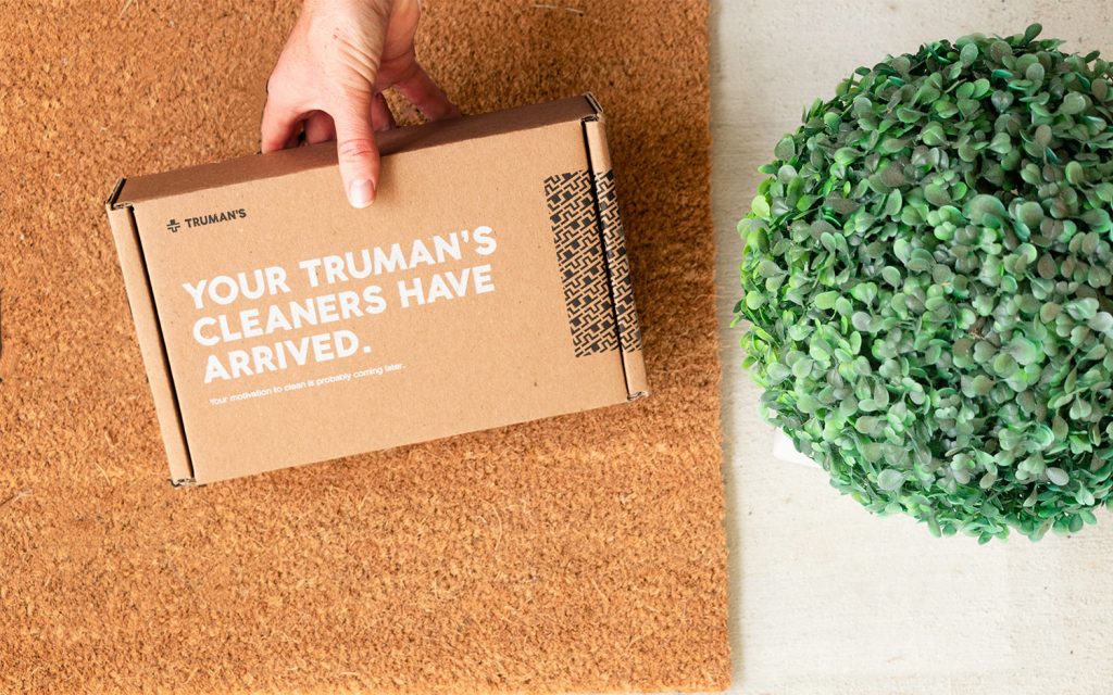 Hand setting a cardboard delivery box on a doormat beside a boxwood sphere