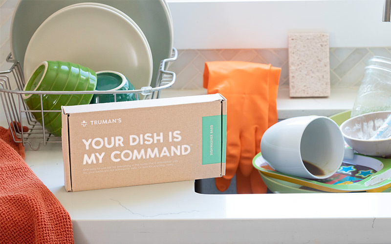 Green and white dishes on a rack beside a product card and orange towel