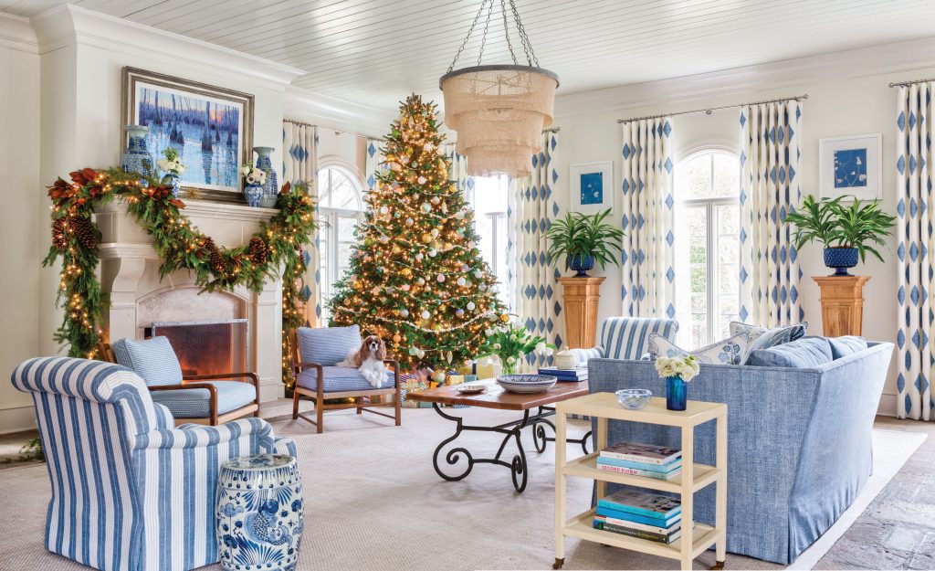 Living room with striped chairs, a lit tree and garlanded mantel