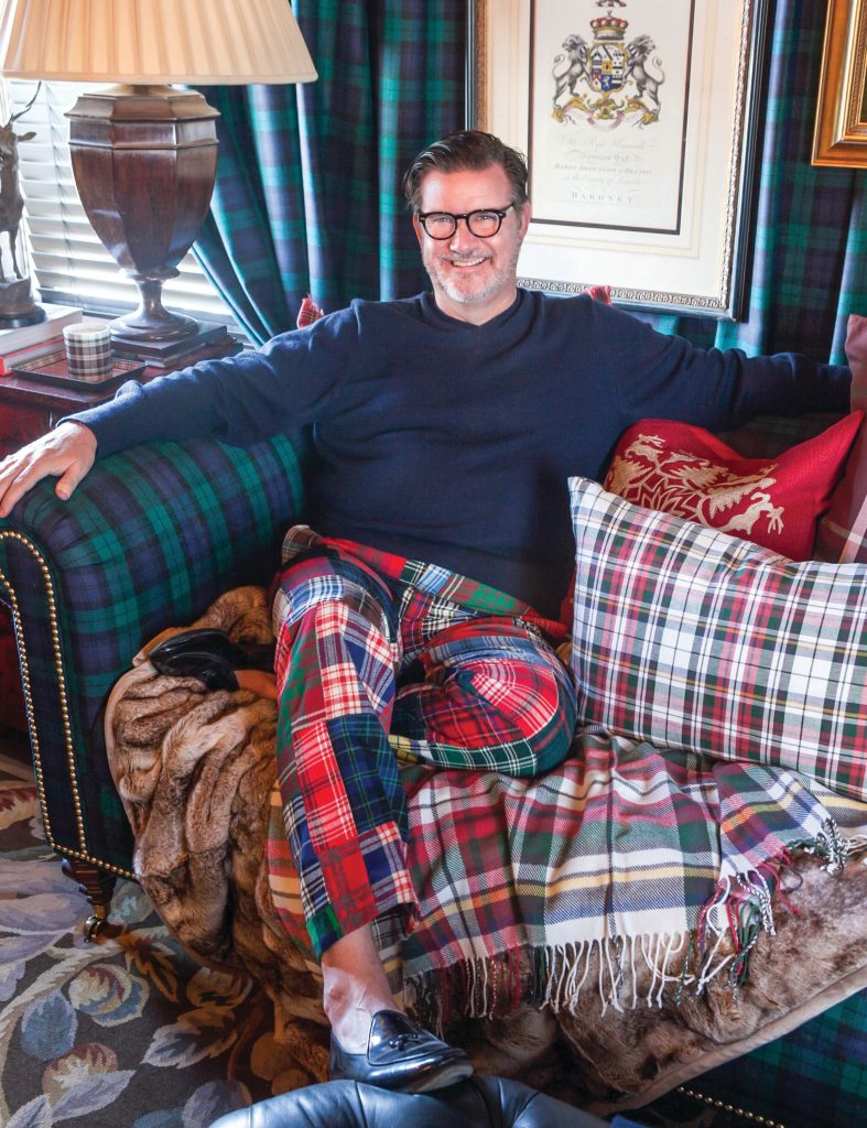 Man in tartan trousers seated on a sofa layered with plaid pillows