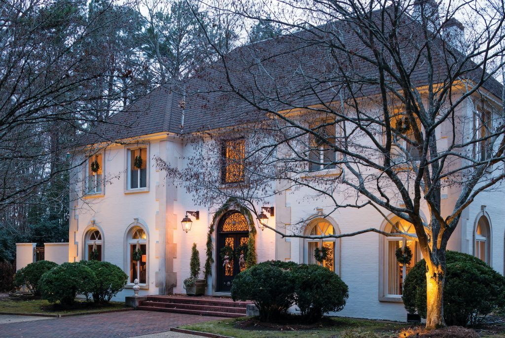 White stucco house lit at dusk with arched windows and boxwoods
