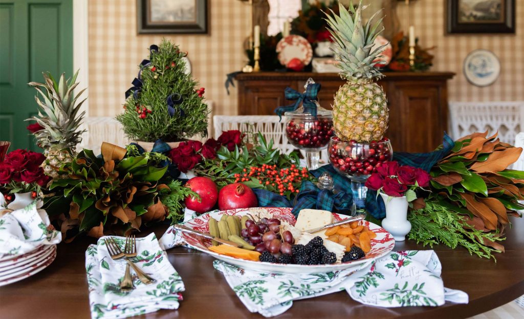 Table centrepiece of pineapple, pomegranates and magnolia on a checked wall