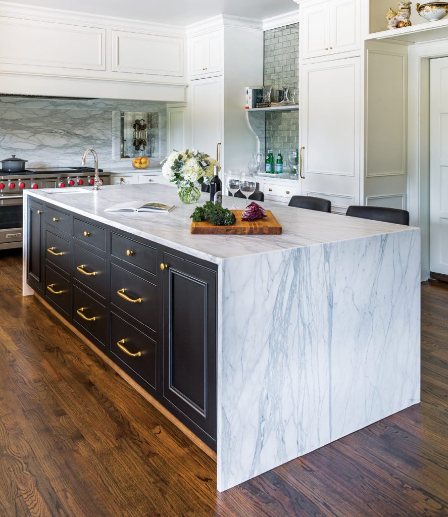 Kitchen with a navy island, brass hardware and marble waterfall counter