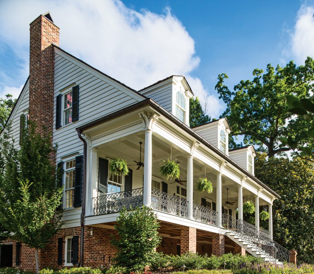 Grey house with a wraparound porch and a tall brick chimney