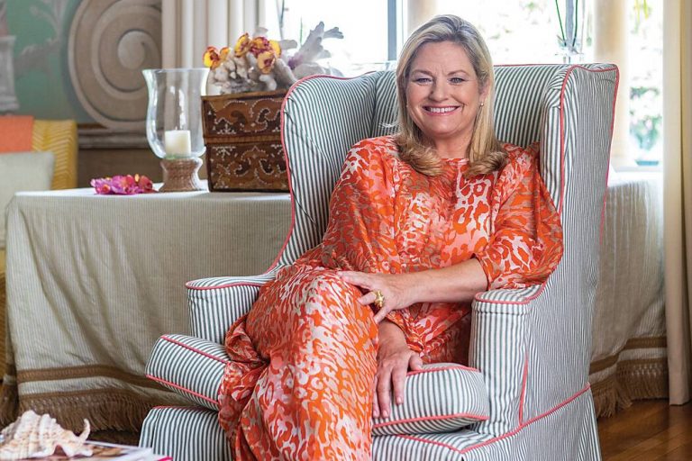 Woman in an orange printed dress seated in a striped wing chair