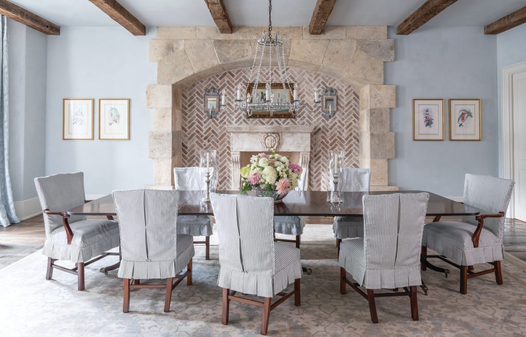 Dining room with slipcovered chairs and a stone fireplace under beams