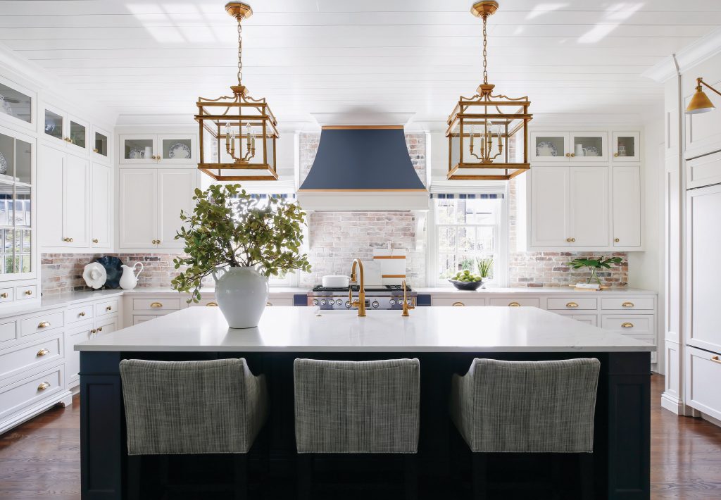 White kitchen with a navy island, brass lanterns and grey stools