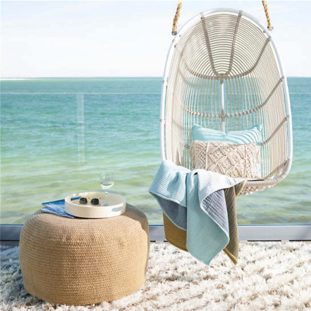 Hanging rattan chair and woven pouf on a beach terrace