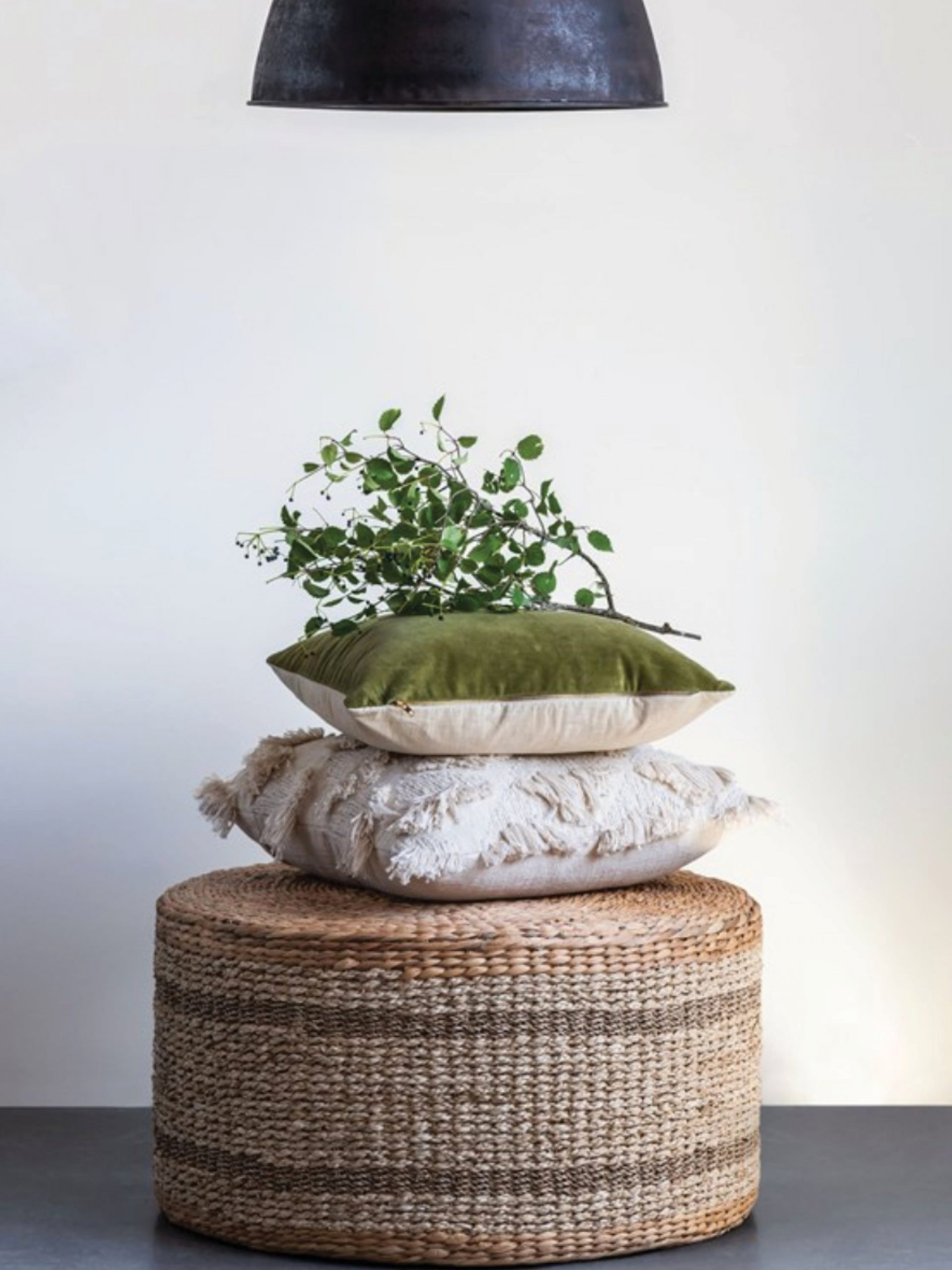 Stacked woven poufs with cushions below a black pendant