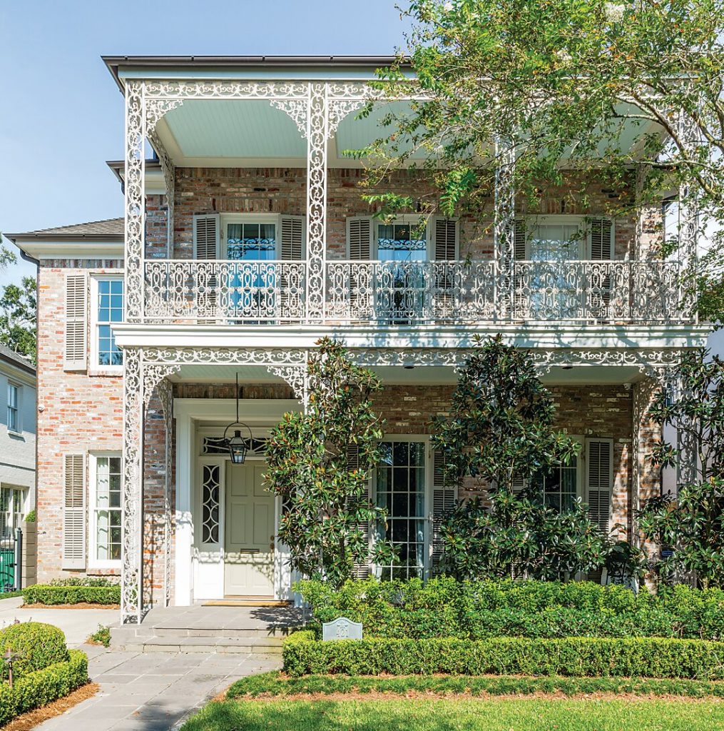 Two-story house with tiered ironwork balconies behind clipped hedges