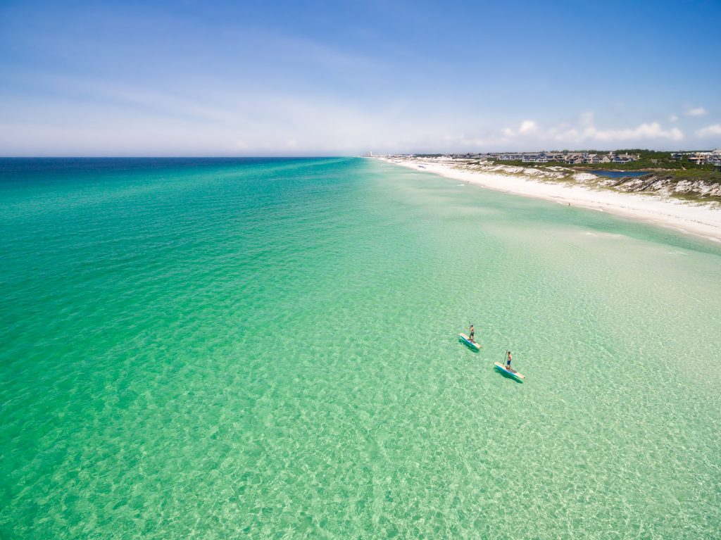 Aerial view of turquoise water and a white sand beach with paddleboarders