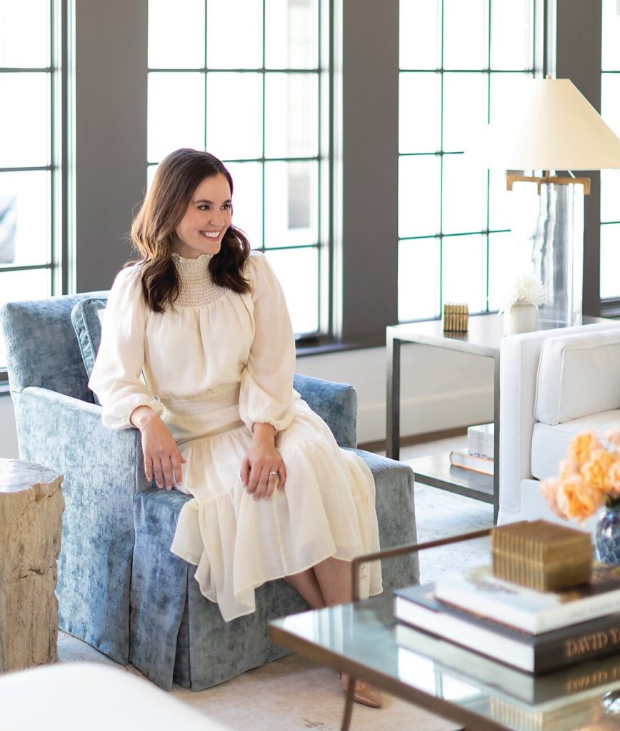 Woman in cream seated in a blue patterned armchair by a steel window