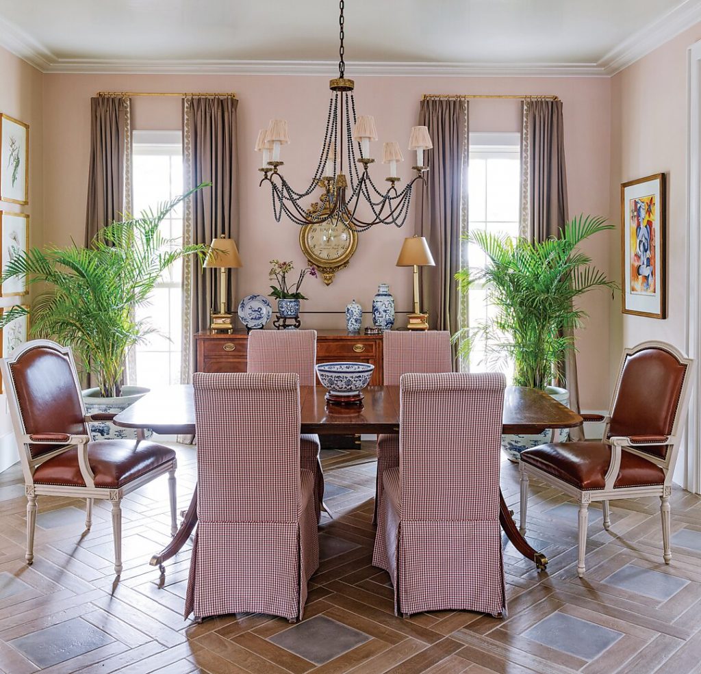 Blush dining room with a gilt chandelier, cane chairs and potted palms