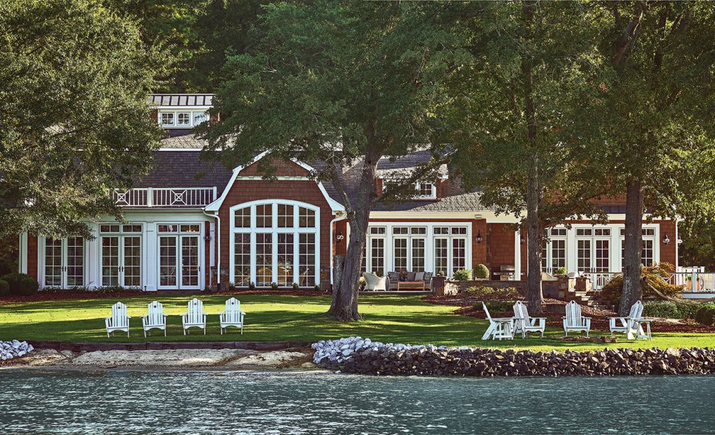 Brick house across a lawn set with white Adirondack chairs