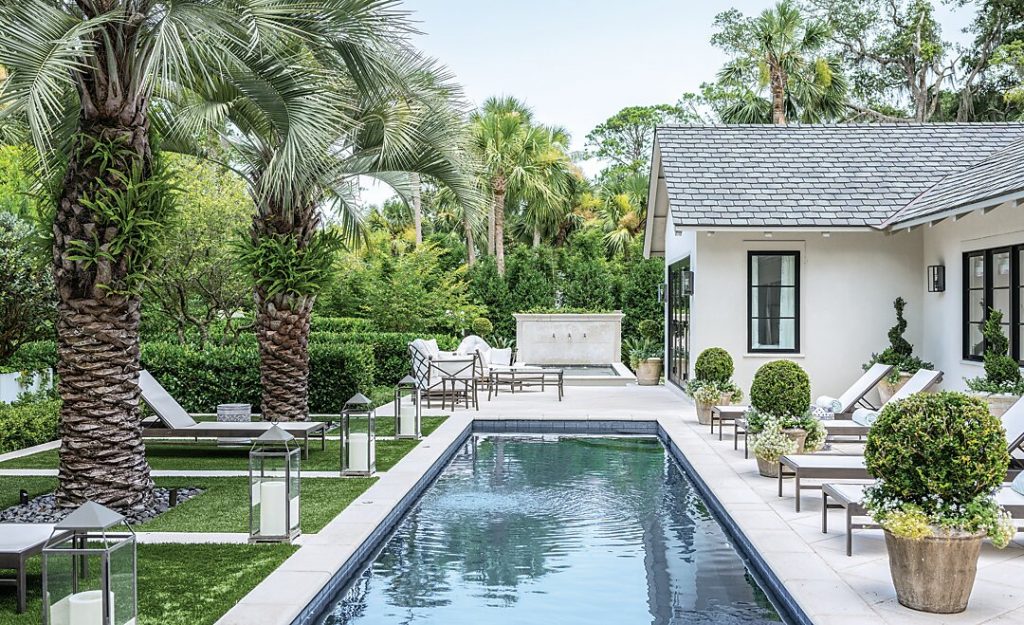 Lap pool bordered by palms and loungers beside a white pool house