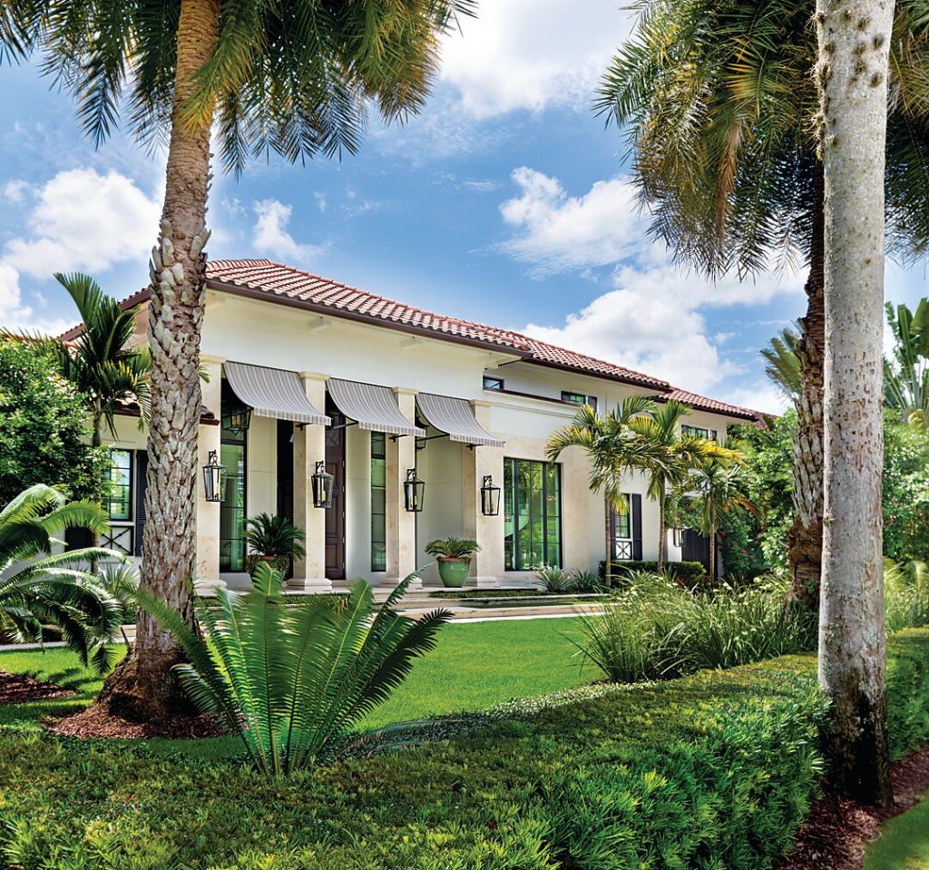 Stucco house with arched loggias behind palms and tropical planting